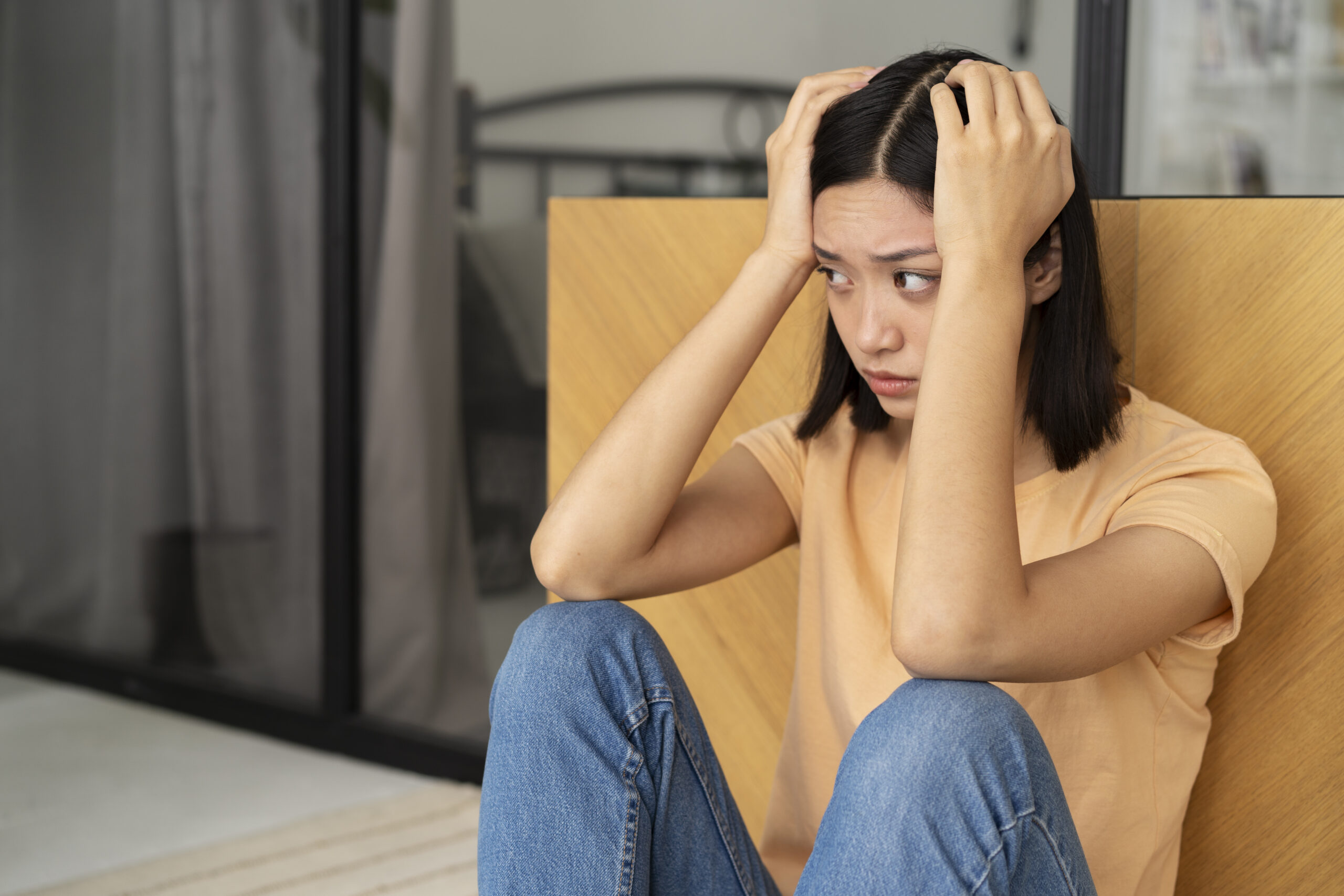 ผู้หญิงนั่งกุมขมับจากอาการปวดศีรษะ ซึ่งอาจเกี่ยวข้องกับความเครียดสะสม